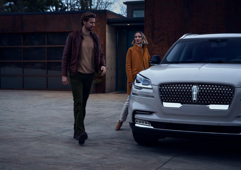 A man and a woman approaching a 2024 Lincoln Aviator® SUV, which illuminates certain lights when they are close | White's Canyon Motors - Lincoln in Spearfish SD